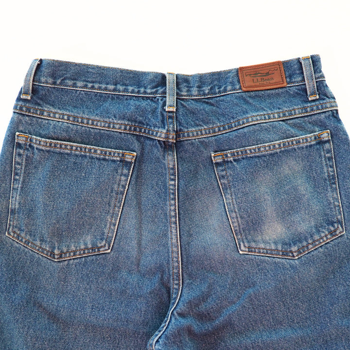 Back view focusing on the pockets of a pair of blue jeans with a brand label on a white background