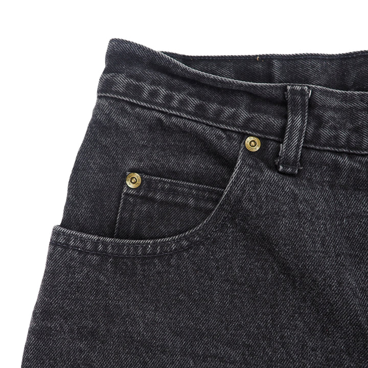Close-up of black denim jeans with gold rivets and black stitching on a white background