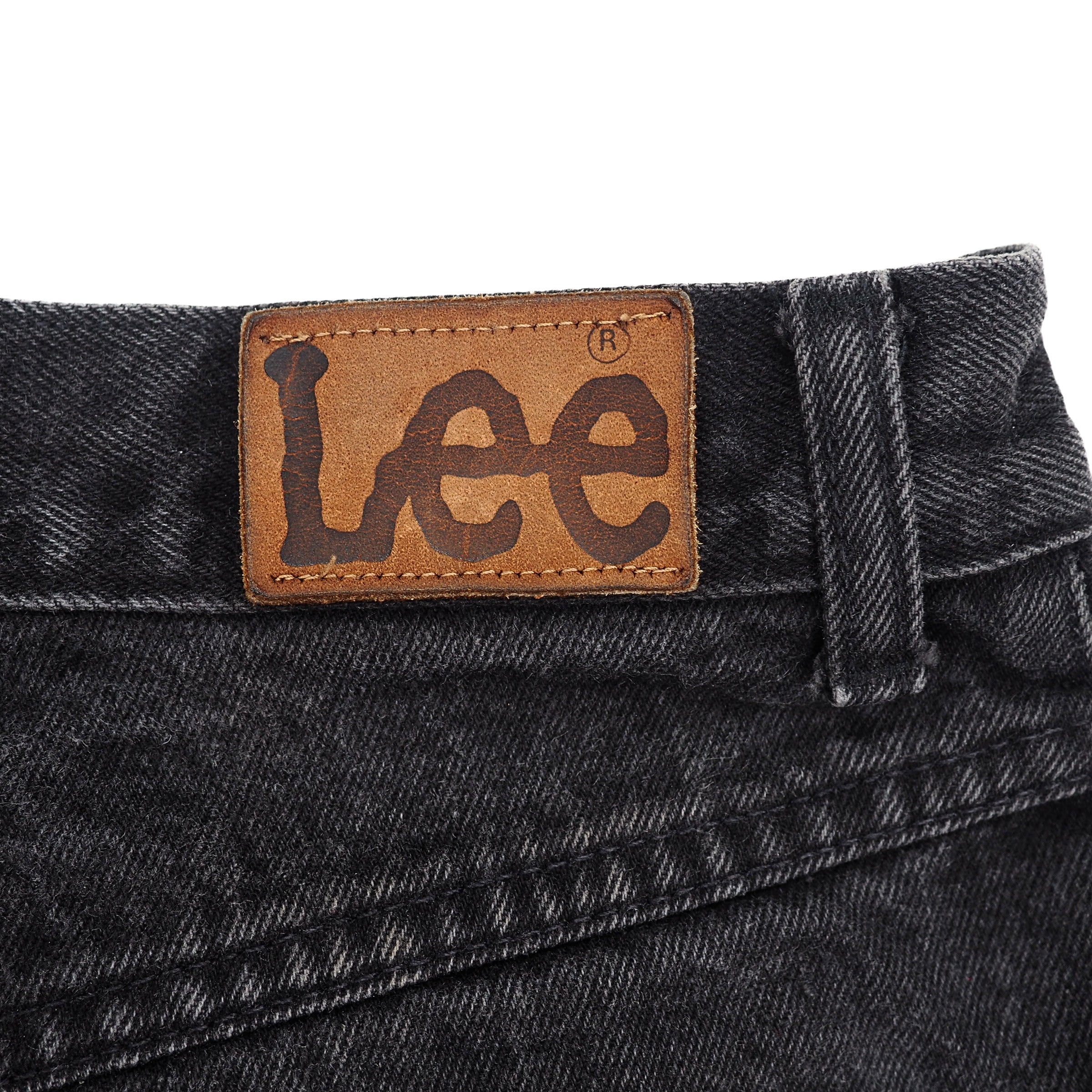 Close-up of a black denim Lee jeans rear waistband with a leather 'Lee' jacron patch on a white background