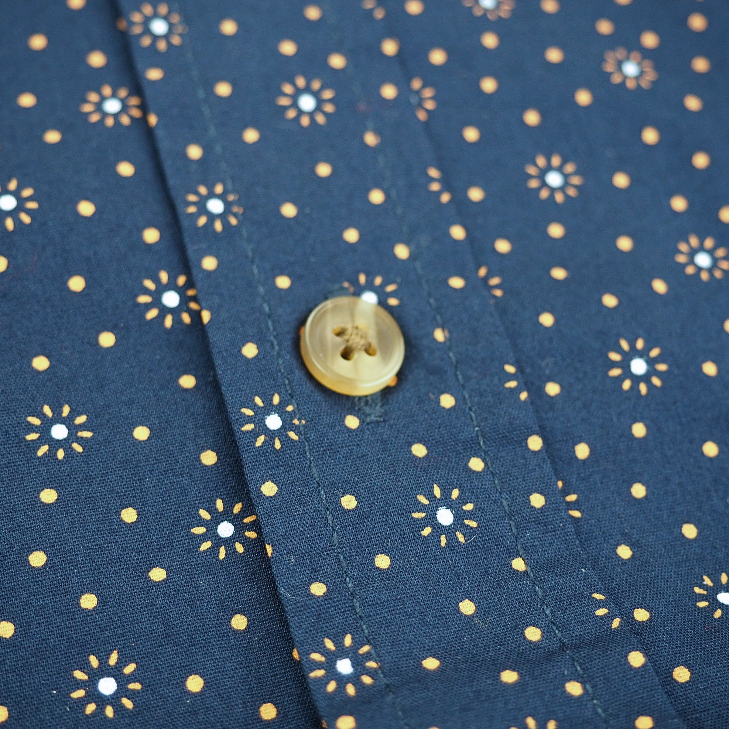 Close-up of a button on blue fabric with gold floral patterns