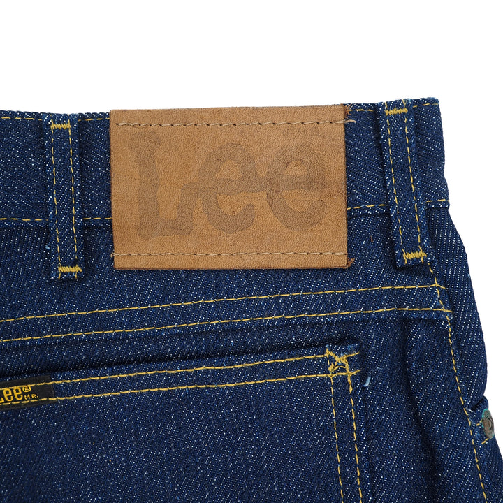 Close-up of a leather 'Lee' jacron patch on a pair of raw indigo denim jeans with a white background