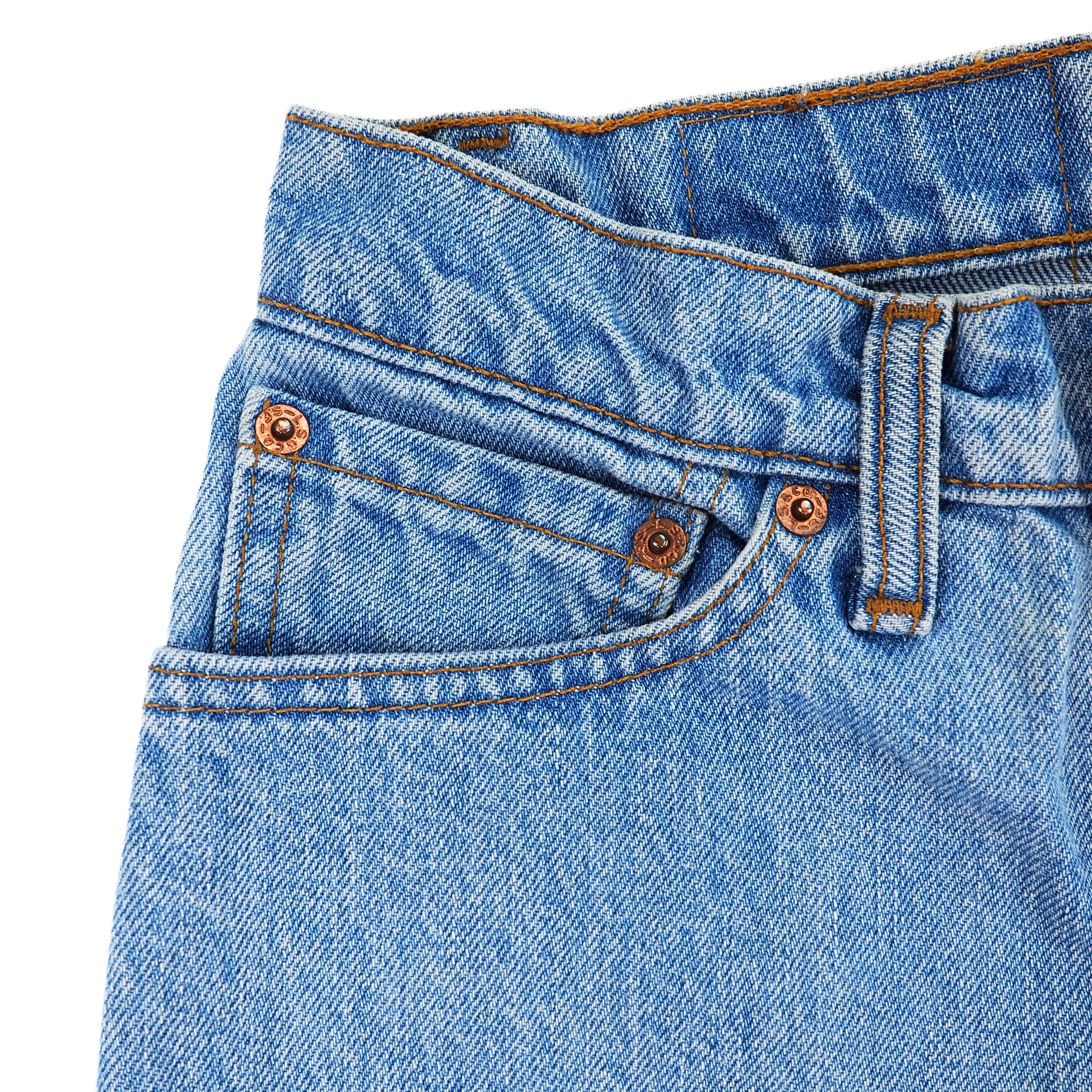 Close-up of blue denim jeans coin pocket area with rivets and stitching details on a white background
