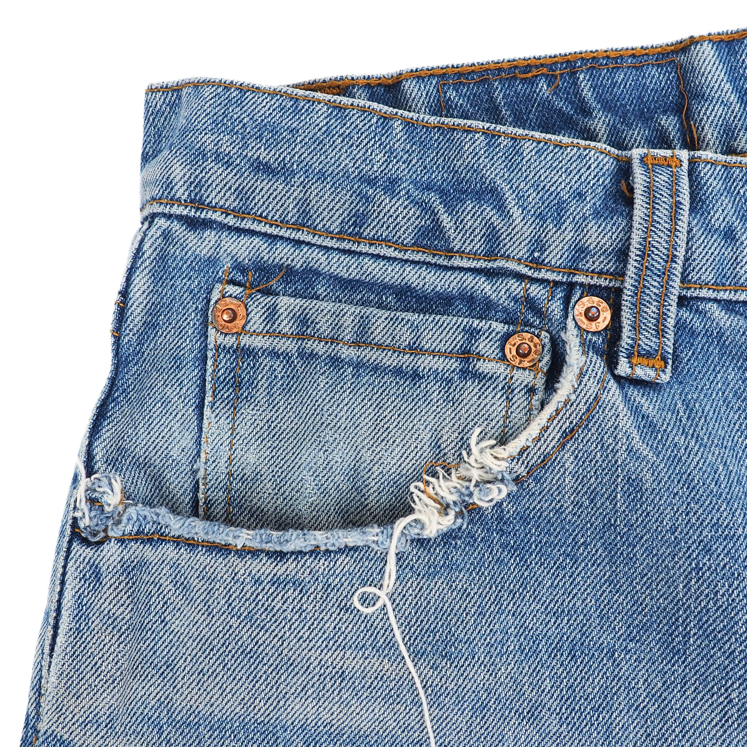 Close-up of blue jeans coin pocket area with fraying and stitching details on a white background