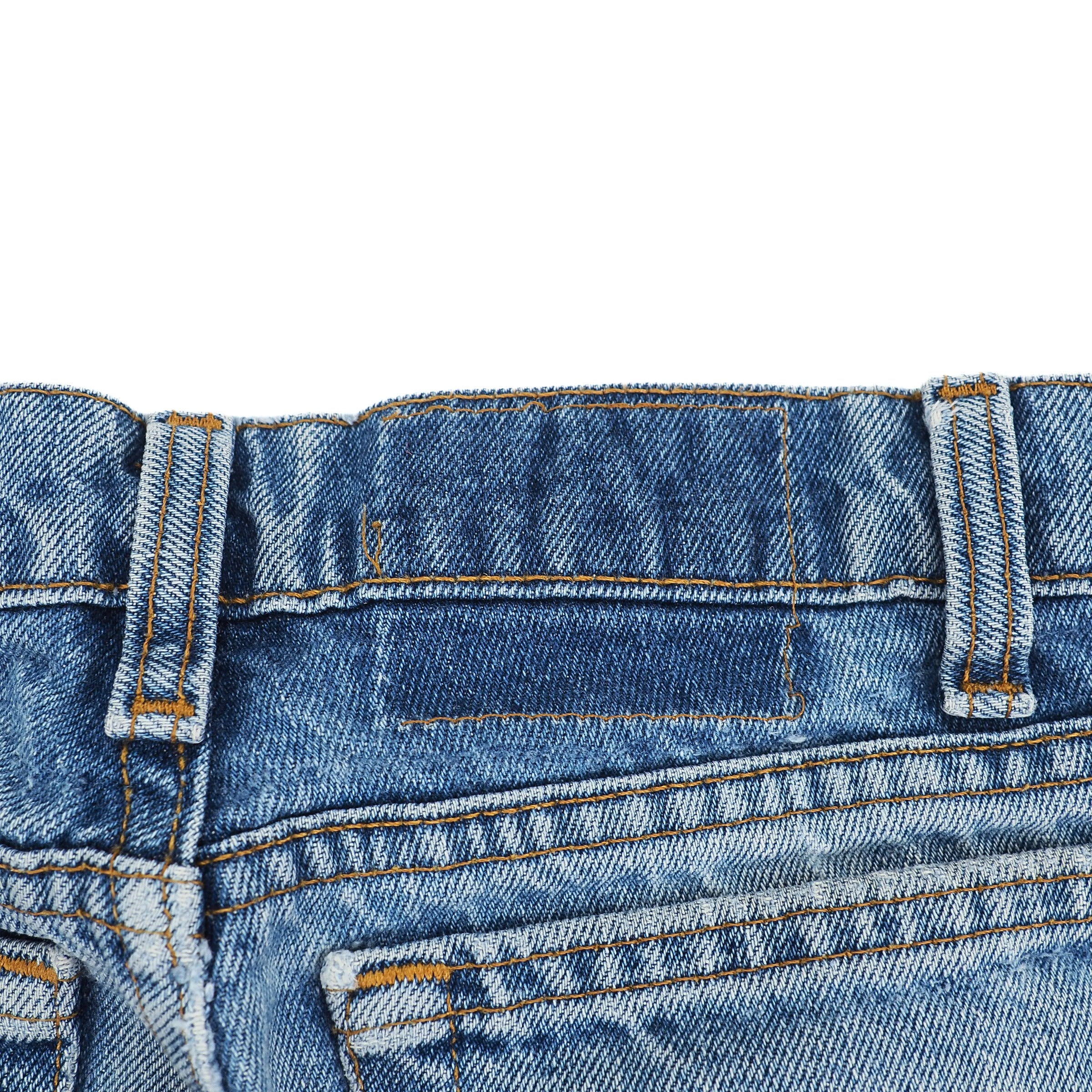 Close-up of blue denim jeans waist area with stitching details on a white background