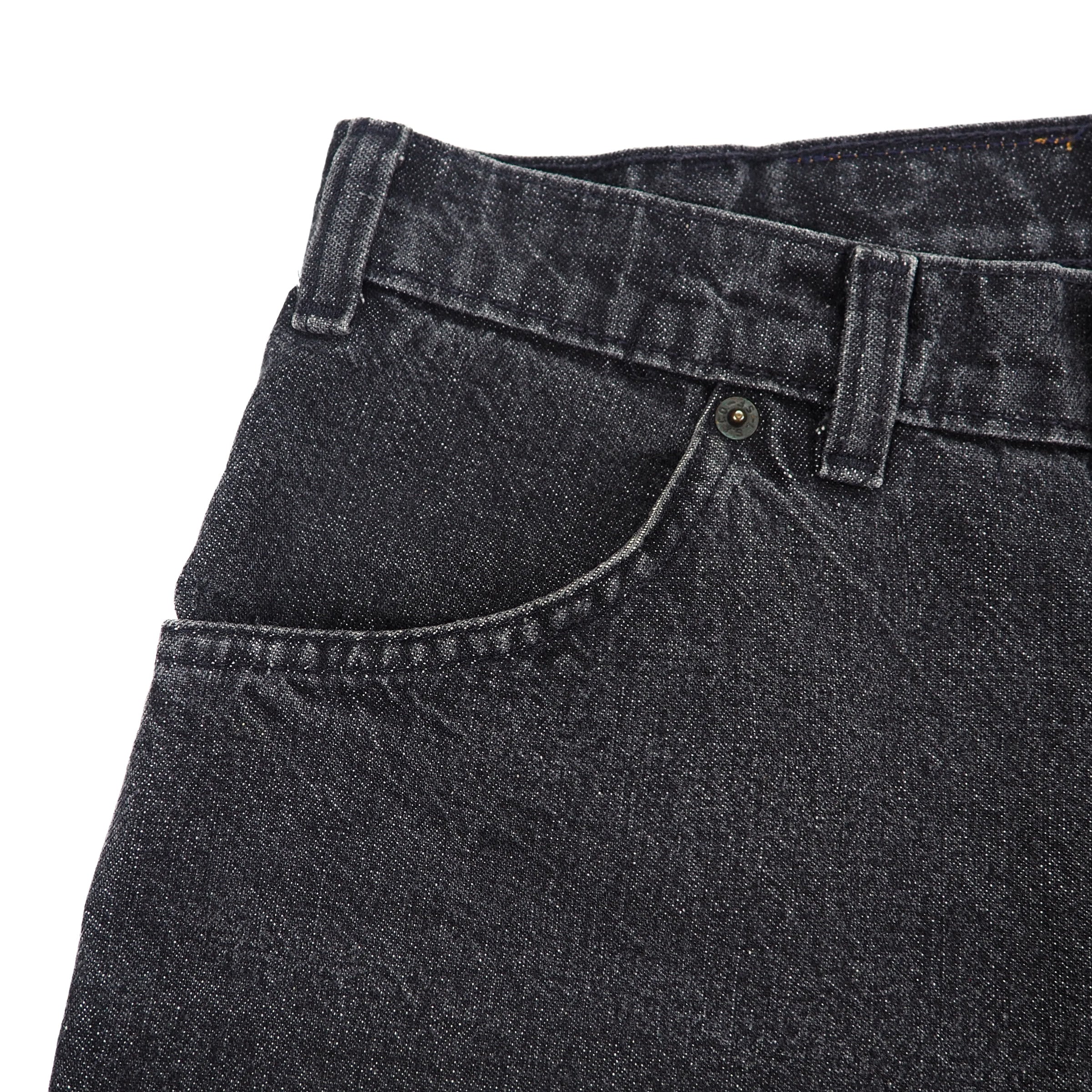 Close-up of black denim jeans with a focus on the waistband and pocket.