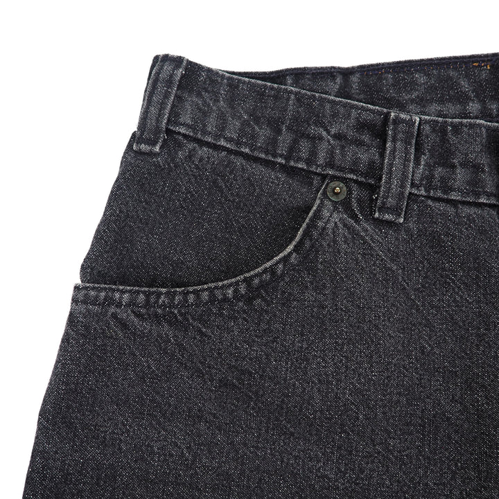 Close-up of black denim jeans with a focus on the waistband and pocket.