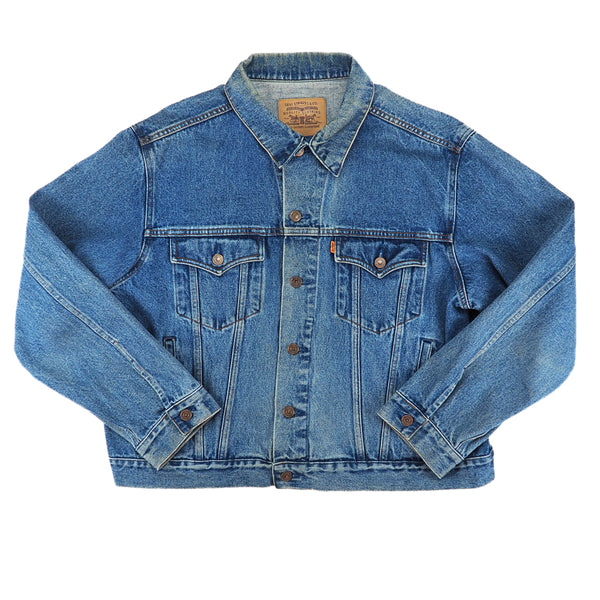 A classic medium-wash blue denim trucker jacket with button-front closure, chest flap pockets, and buttoned cuffs, laid flat against a white background.