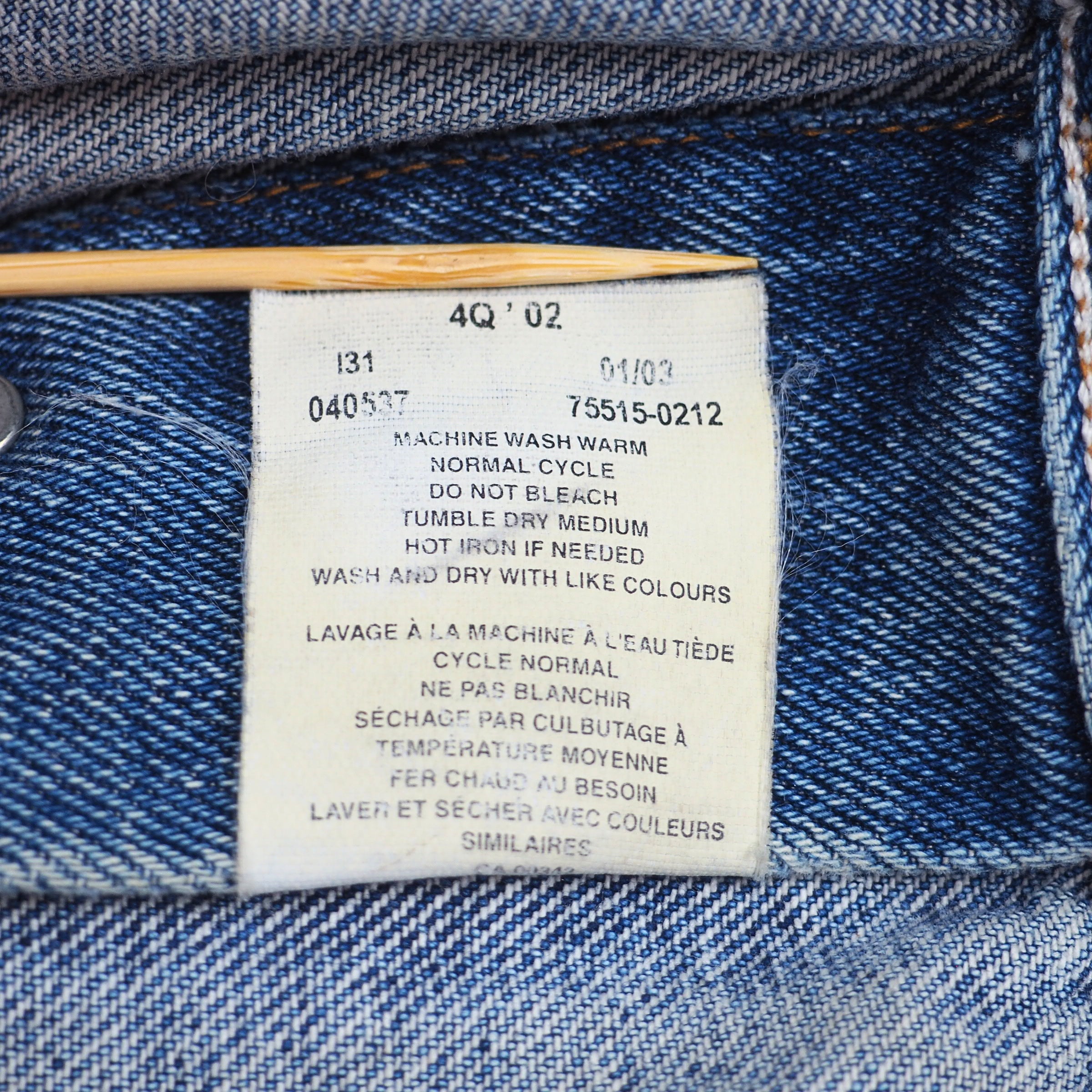 Close-up of a blue denim garment's inner label area, showing printed care instructions in English and French on a white tag held by a wooden stick.