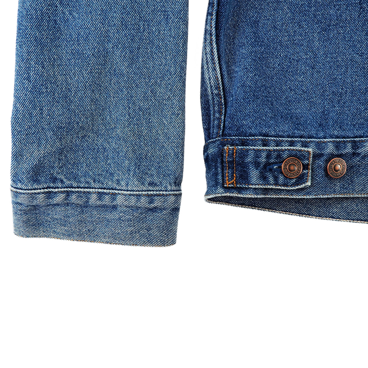 Close-up detail of a blue denim garment showing the cuffed sleeve and the rolled hem with metal snap buttons and contrast stitching.