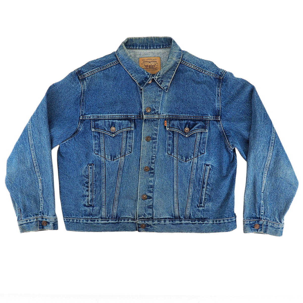 A classic blue denim trucker jacket with button closures, chest flap pockets, and a leather brand patch on the collar, displayed flat against a white background.