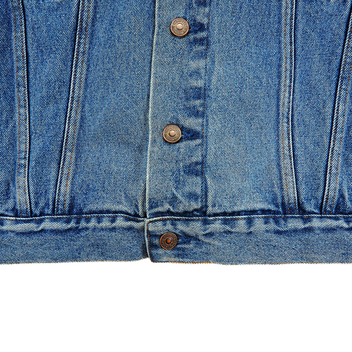 Close-up of a blue denim jacket showing the front button closure with brown buttons and the detailed twill texture of the denim fabric.