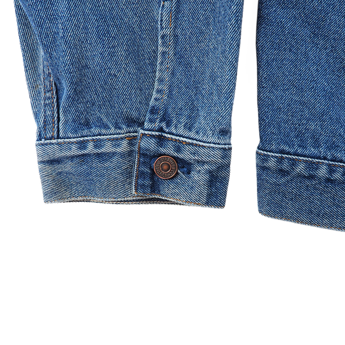 Close-up detail of blue denim jeans showing the cuff of one leg with a single brown button closure, alongside the hem of another leg, on a plain white background.
