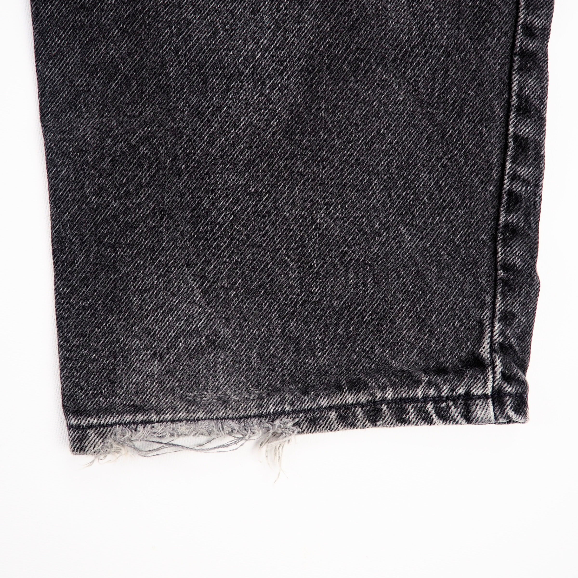 Close-up of a black denim fabric with frayed edge on a white background