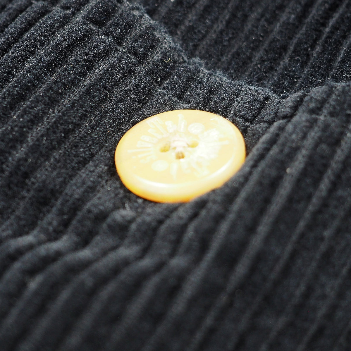 Close-up of a black ribbed corduroy fabric with a round pale yellow button featuring the branding 'silverTab'.