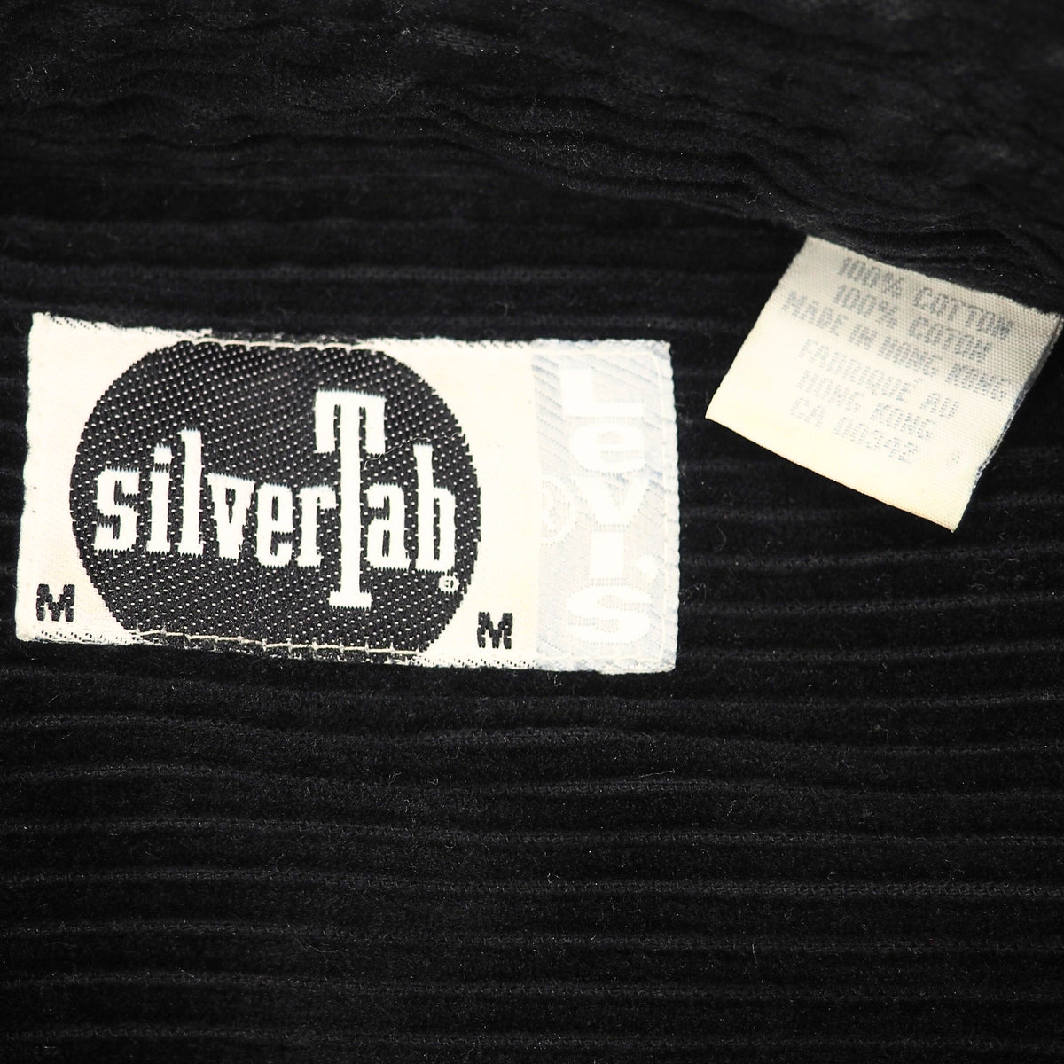 Close-up of a black ribbed fabric garment showing two sewn-in labels: a larger white and black silverTab label and a smaller white care tag.