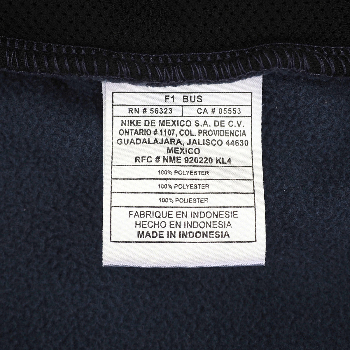 Close-up of a white product care label sewn onto dark navy mesh fabric, showing Nike branding and manufacturing details.