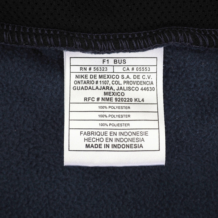 Close-up of a white product care label sewn onto dark navy mesh fabric, showing Nike branding and manufacturing details.