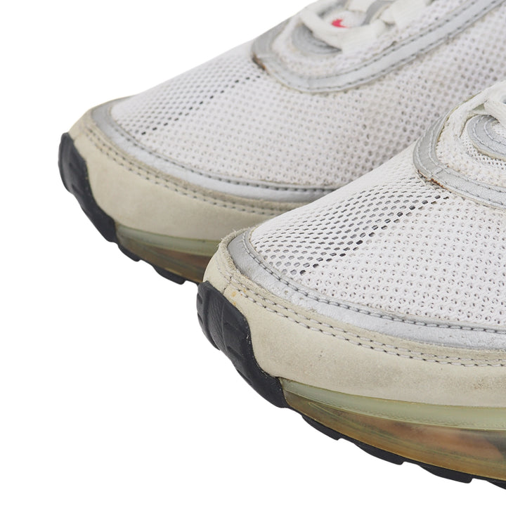 Close up of the toe area of a pair of white mesh sneakers with black soles on a white background