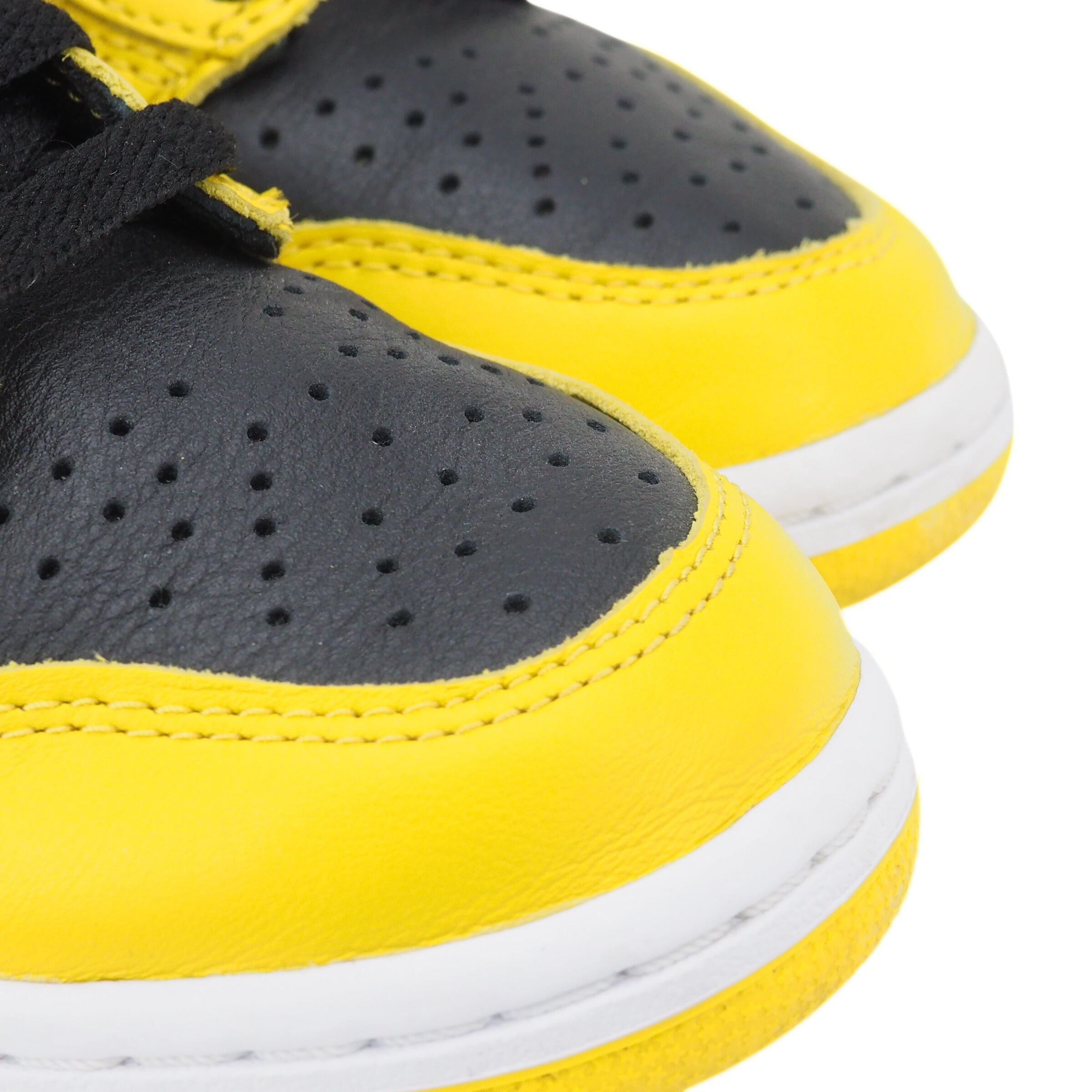 Close-up of the toe area of a pair of black and yellow Nike Dunk basketball sneakers with white soles on a white background