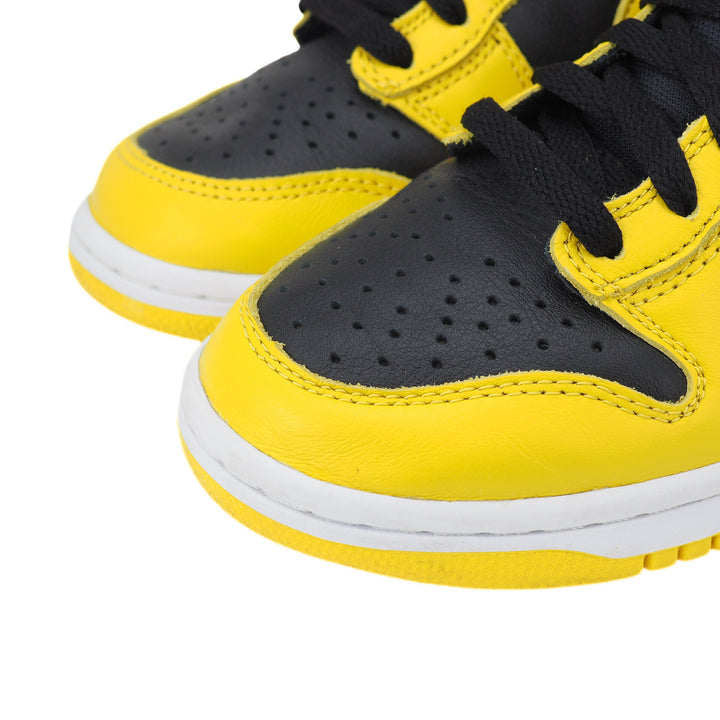 Close up of the toe area of a pair of yellow and black basketball sneakers with white soles on a white background