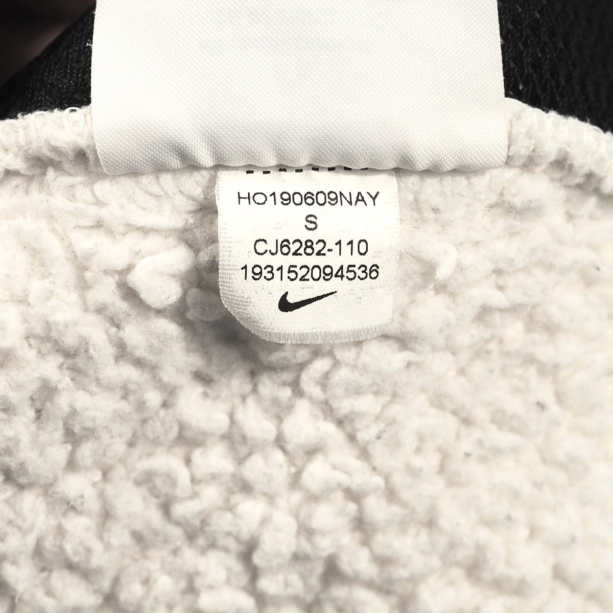 Close-up of a white fleece or sherpa garment label showing printed size and Nike branding with a small black swoosh.
