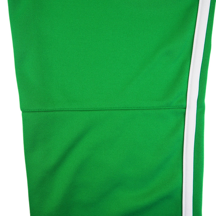 Pant leg detail of a pair of green Nike track pants with white stripes on a white background