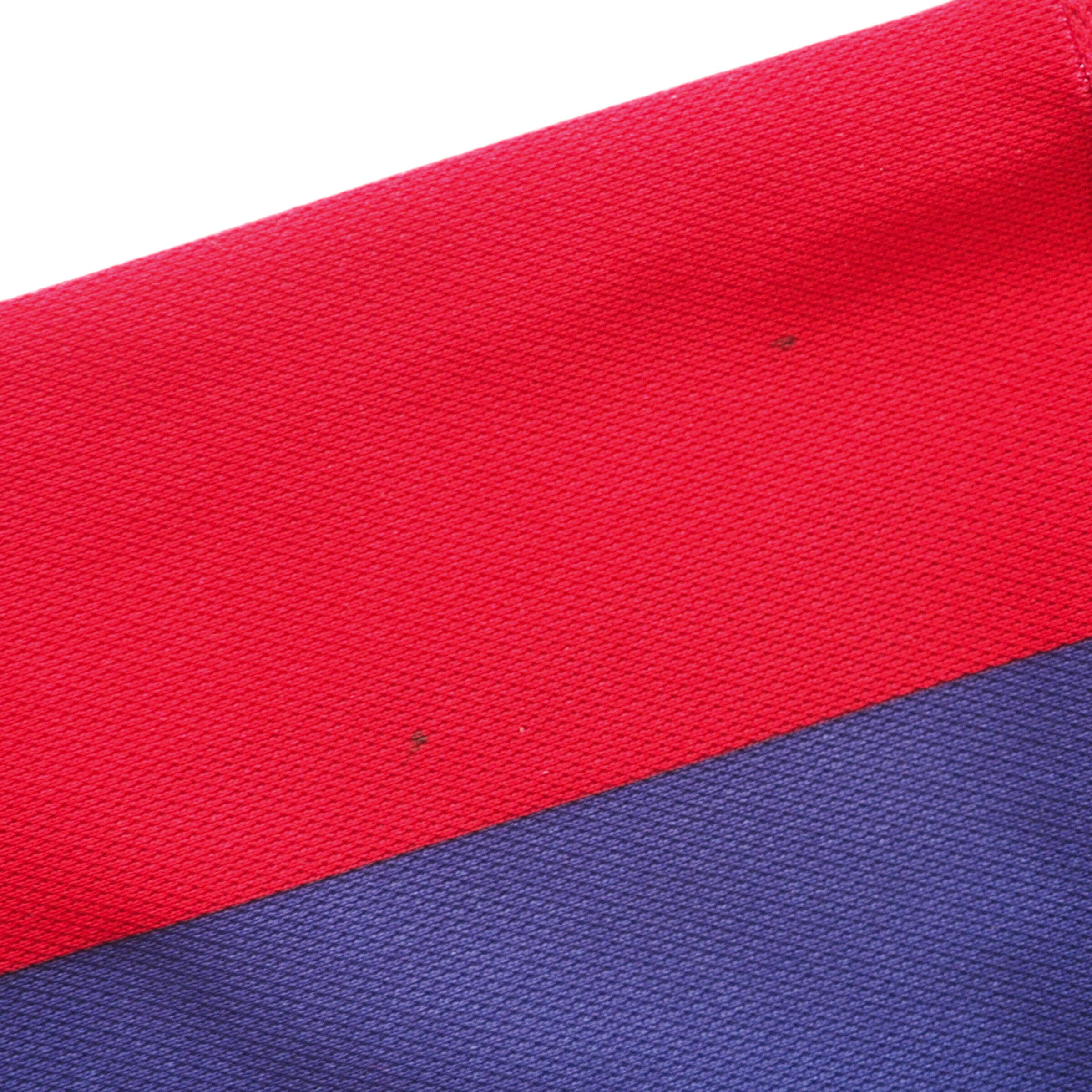 Close-up of red and blue fabric with a textured pattern and detailing two small spot stains on the red portion