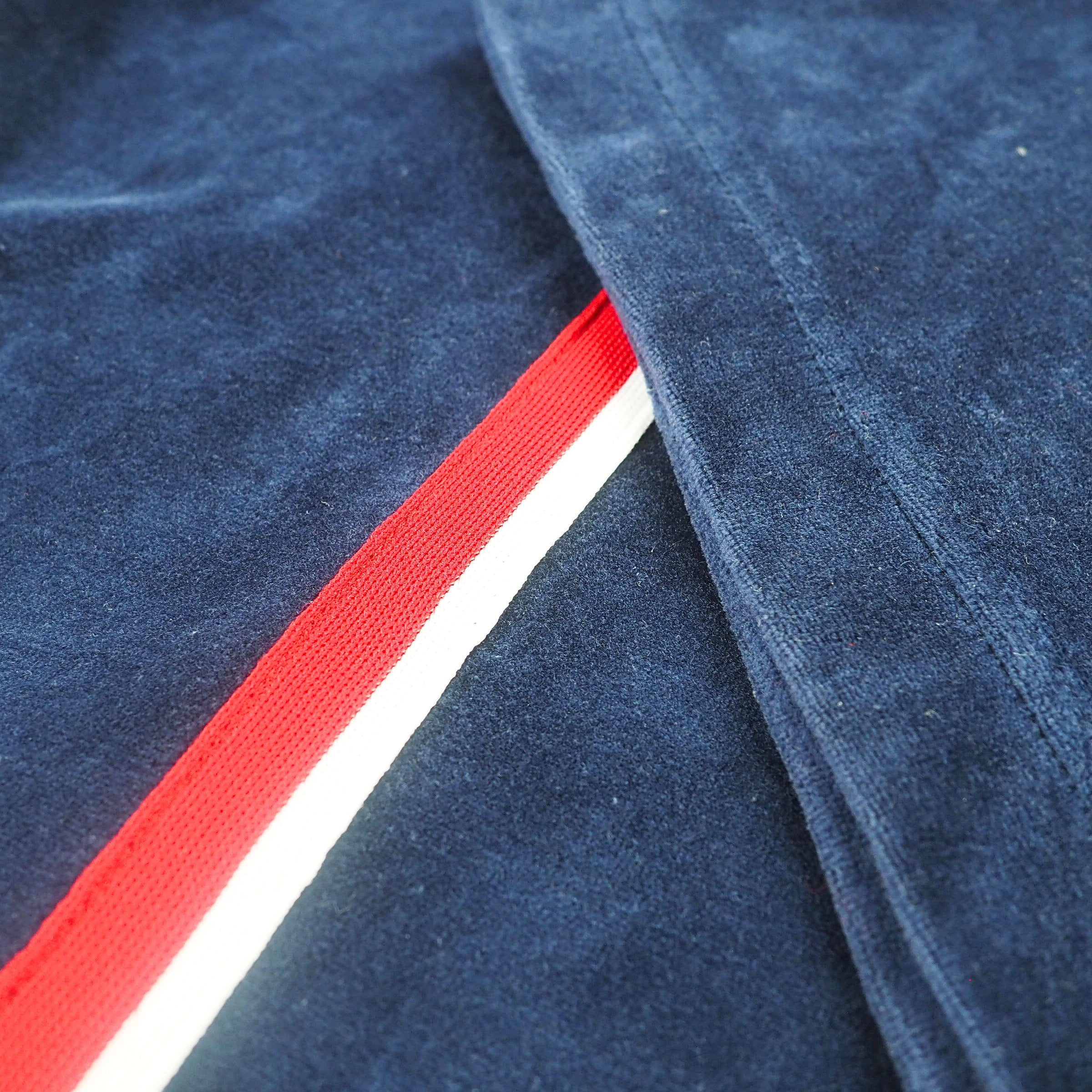 Close up detail of a navy blue velour jacket with a red and white striped trim