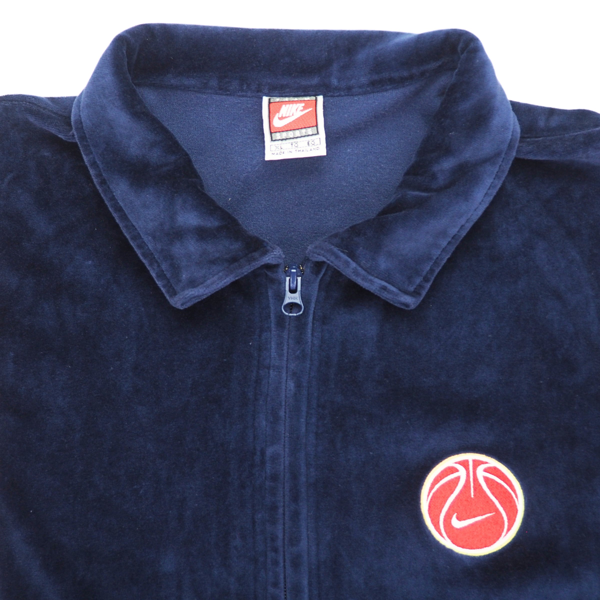 Detail of the collar and basketball patch  of a navy velour basketball jacket on a white background