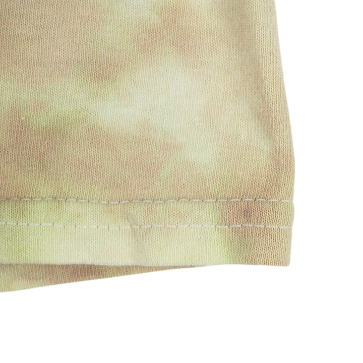 Close-up of a light beige and pale yellow tie-dye fabric with a neat hem and white stitching, set against a plain white background.