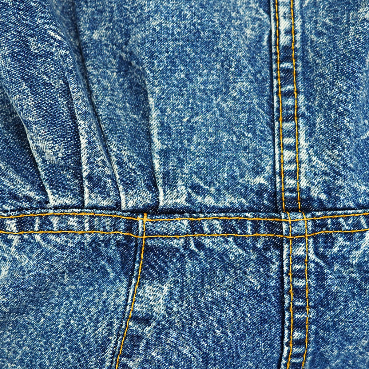Close-up of blue denim fabric with a faded wash and yellow contrast stitching.