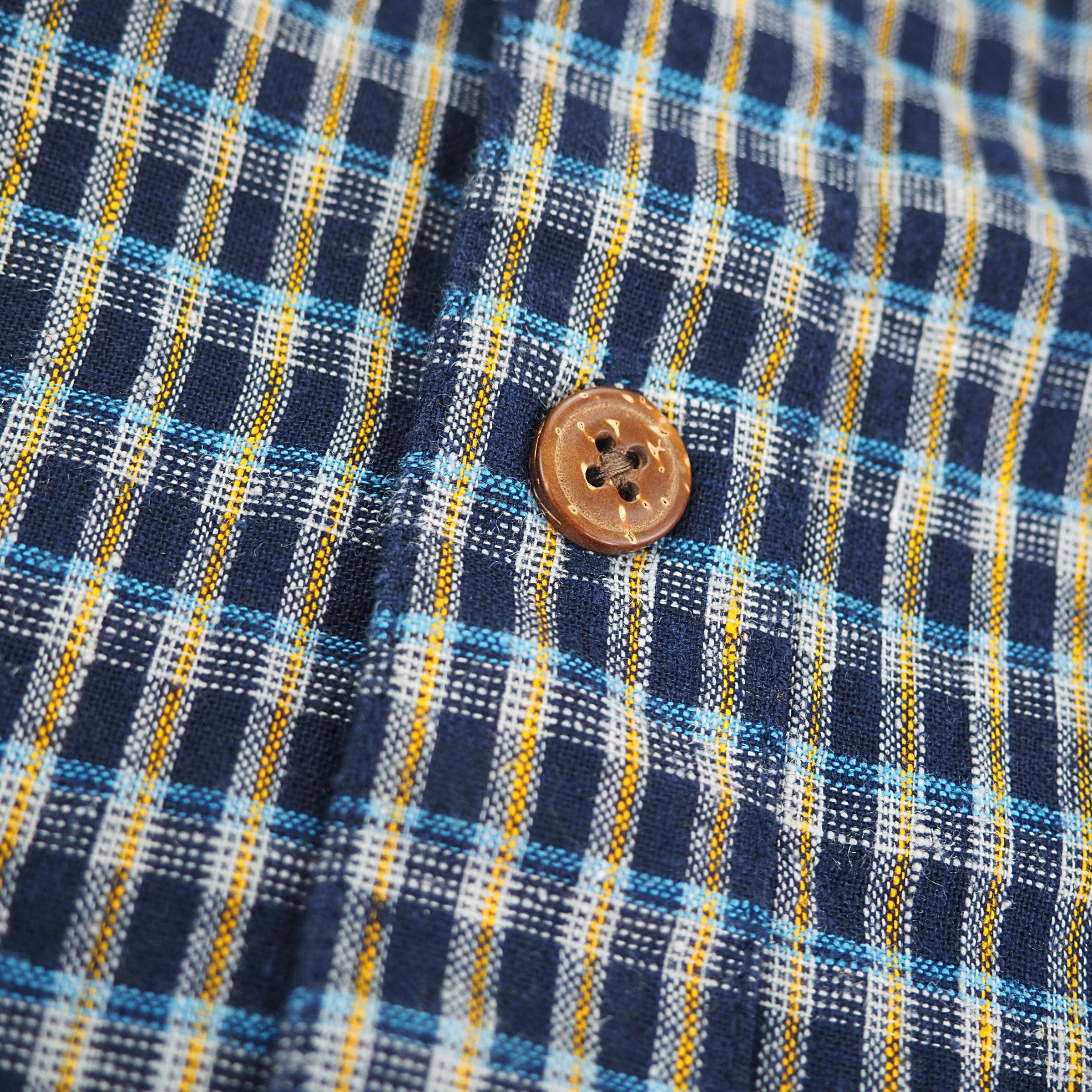 Close-up of a plaid fabric with a button, featuring blue, yellow, and white colors.