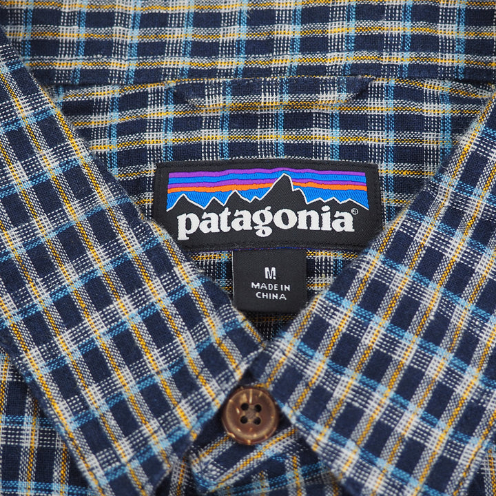 Close-up of a Patagonia label on a plaid shirt with a button.