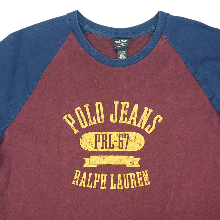 A close-up of a raglan-style long-sleeve shirt with a maroon body and navy blue sleeves. The front has a distressed yellow graphic reading 'POLO JEANS' and 'RALPH LAUREN' with 'PRL-67' in the center.