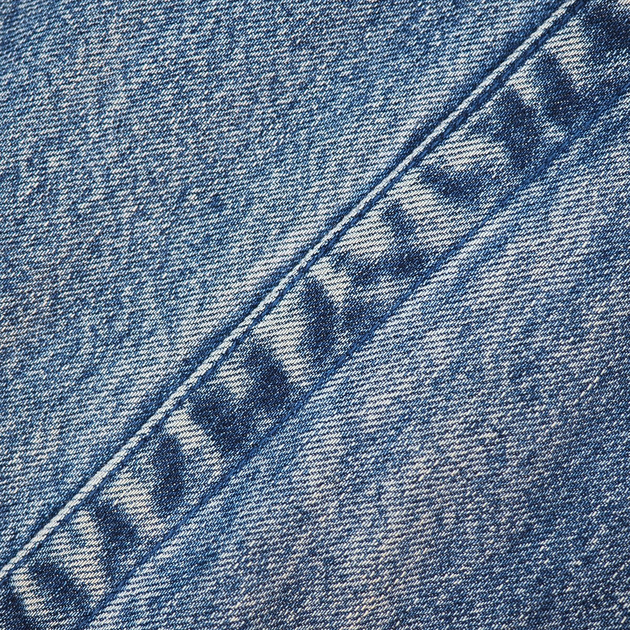 A close-up of blue denim fabric with a diagonal seam and a partially visible embroidered or printed brand mark reading 'HAYABUSA' in dark blue thread.