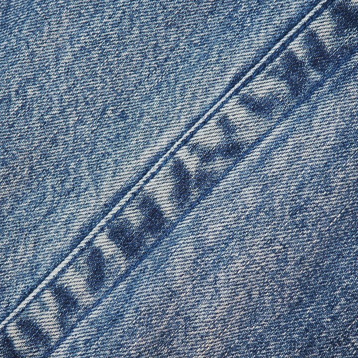 A close-up of blue denim fabric with a diagonal seam and a partially visible embroidered or printed brand mark reading 'HAYABUSA' in dark blue thread.