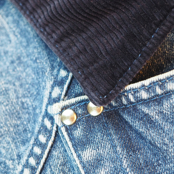 Close-up detail of a dark charcoal corduroy collar layered over blue denim fabric with metal snap buttons.