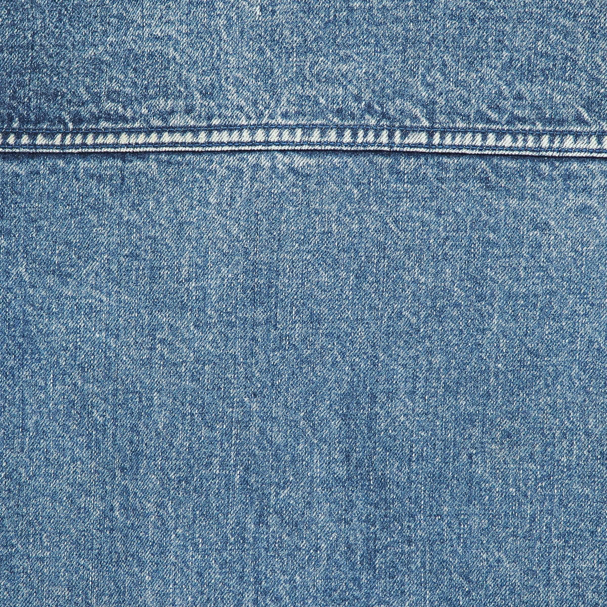 A close-up of blue denim fabric with a horizontal seam and visible weave texture.