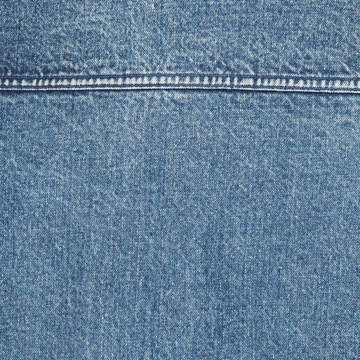 A close-up of blue denim fabric with a horizontal seam and visible weave texture.