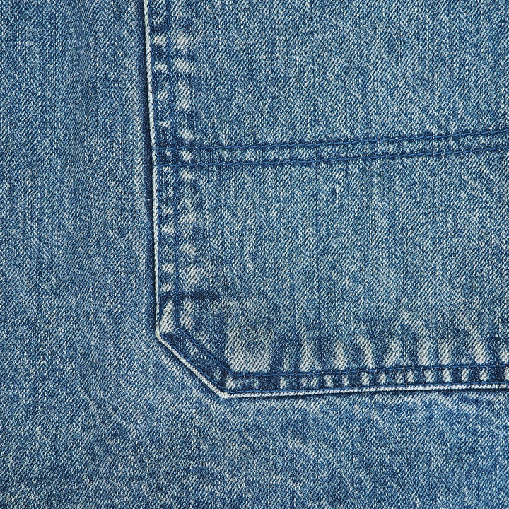 Close-up of a blue denim fabric texture showing the corner of a pocket with detailed stitching.