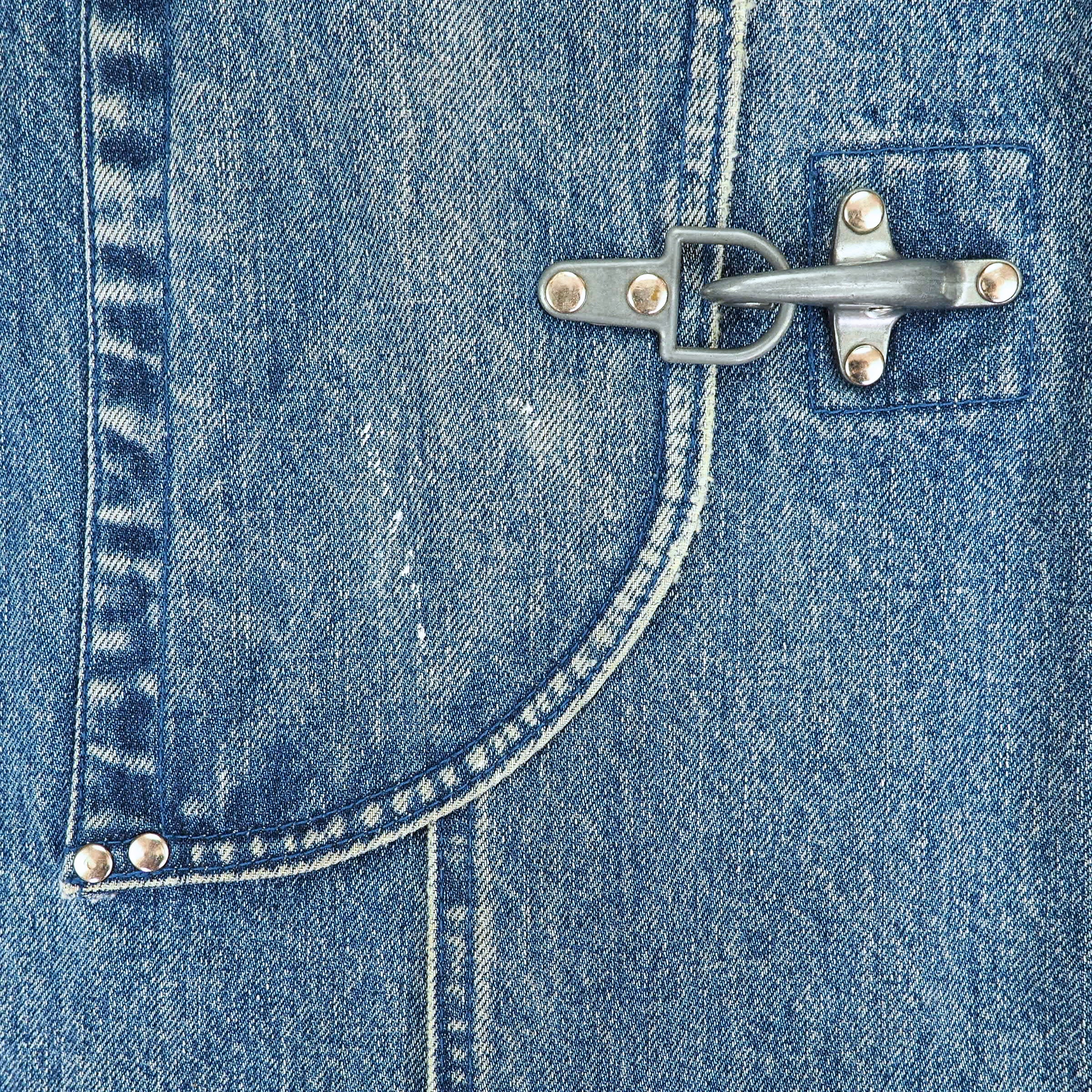 Close-up of a blue denim garment featuring a curved pocket with silver-toned metal snap buttons and a metal toggle clasp.