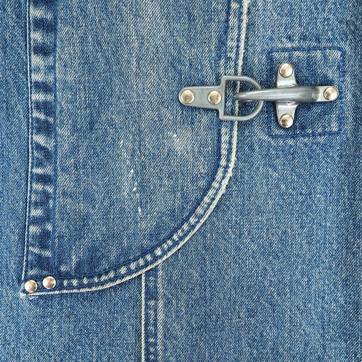 Close-up of a blue denim garment featuring a curved pocket with silver-toned metal snap buttons and a metal toggle clasp.