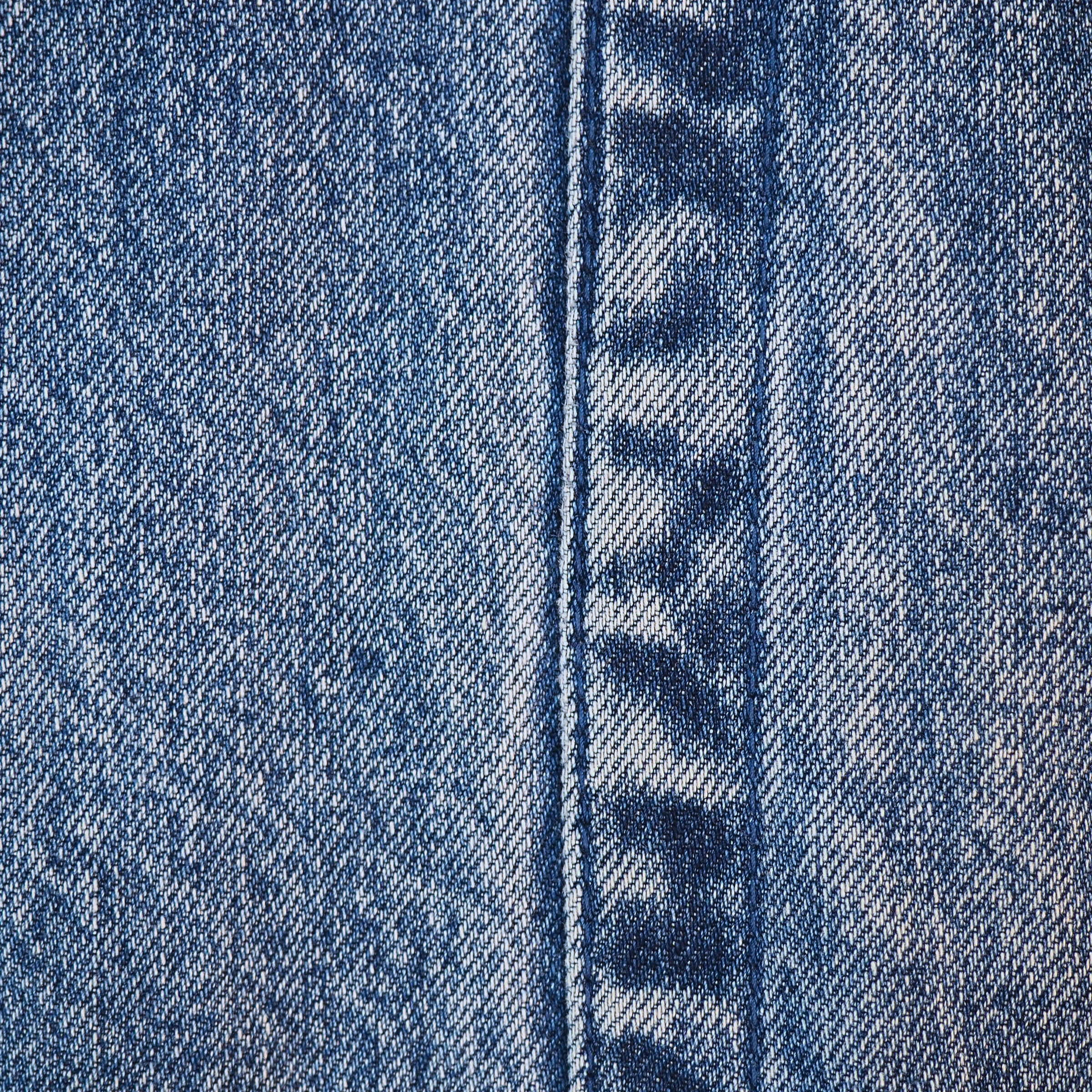 Close-up of blue denim fabric with a central seam and visible twill weave texture.