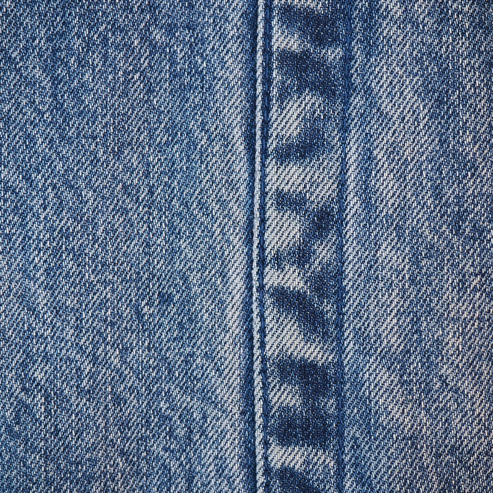 Close-up of blue denim fabric with a central seam and visible twill weave texture.