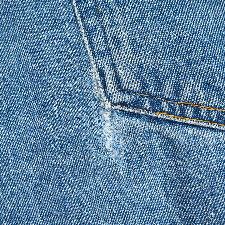 Close-up of blue denim fabric with a tear repair and stitching detail