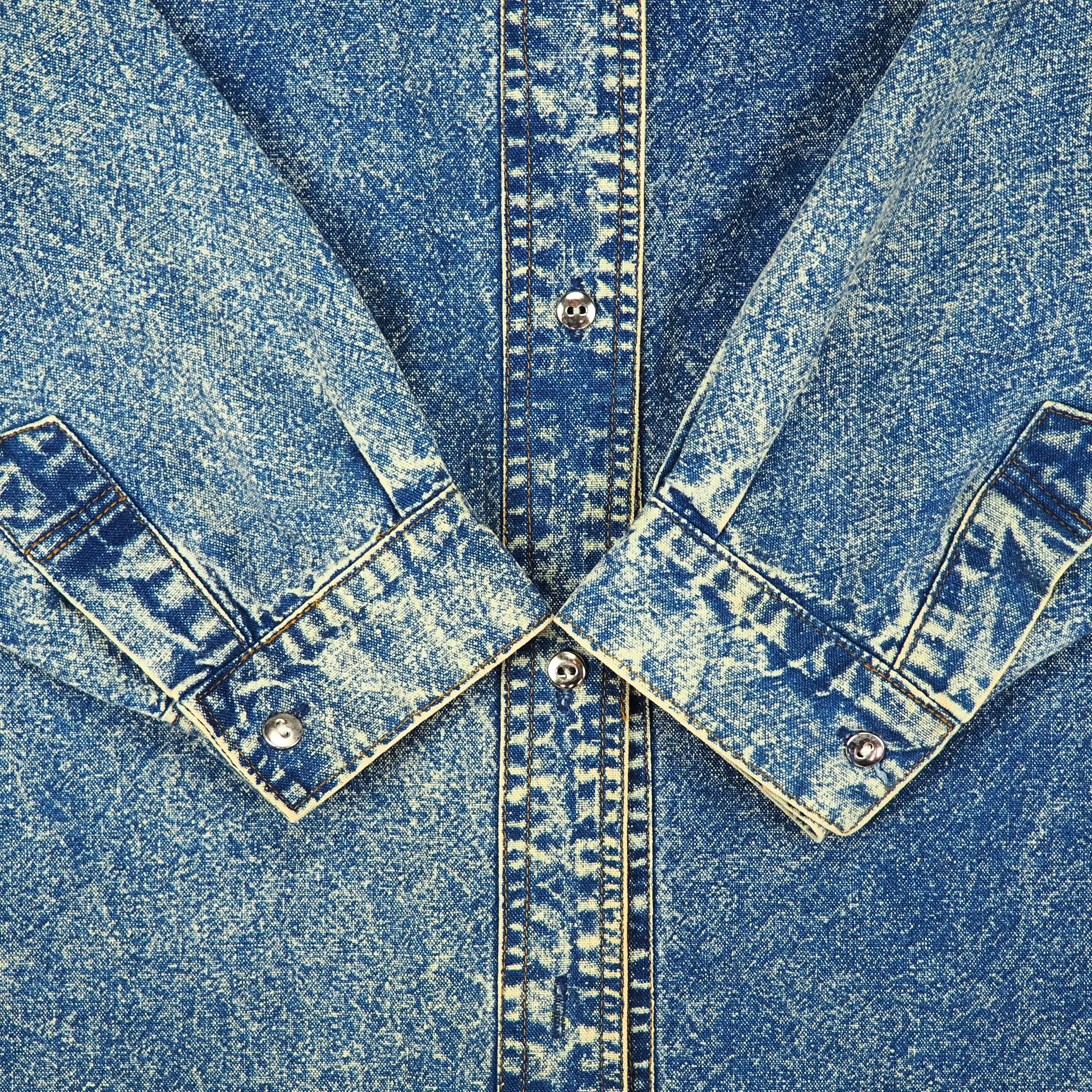 Close-up of a blue acid wash denim shirt with sleeve cuffs folded onto body.