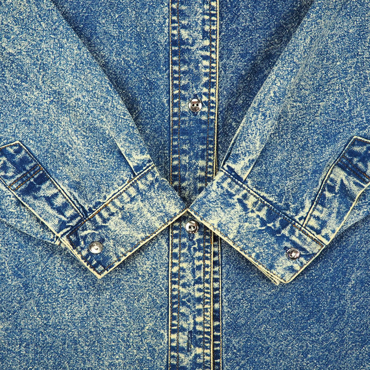 Close-up of a blue acid wash denim shirt with sleeve cuffs folded onto body.