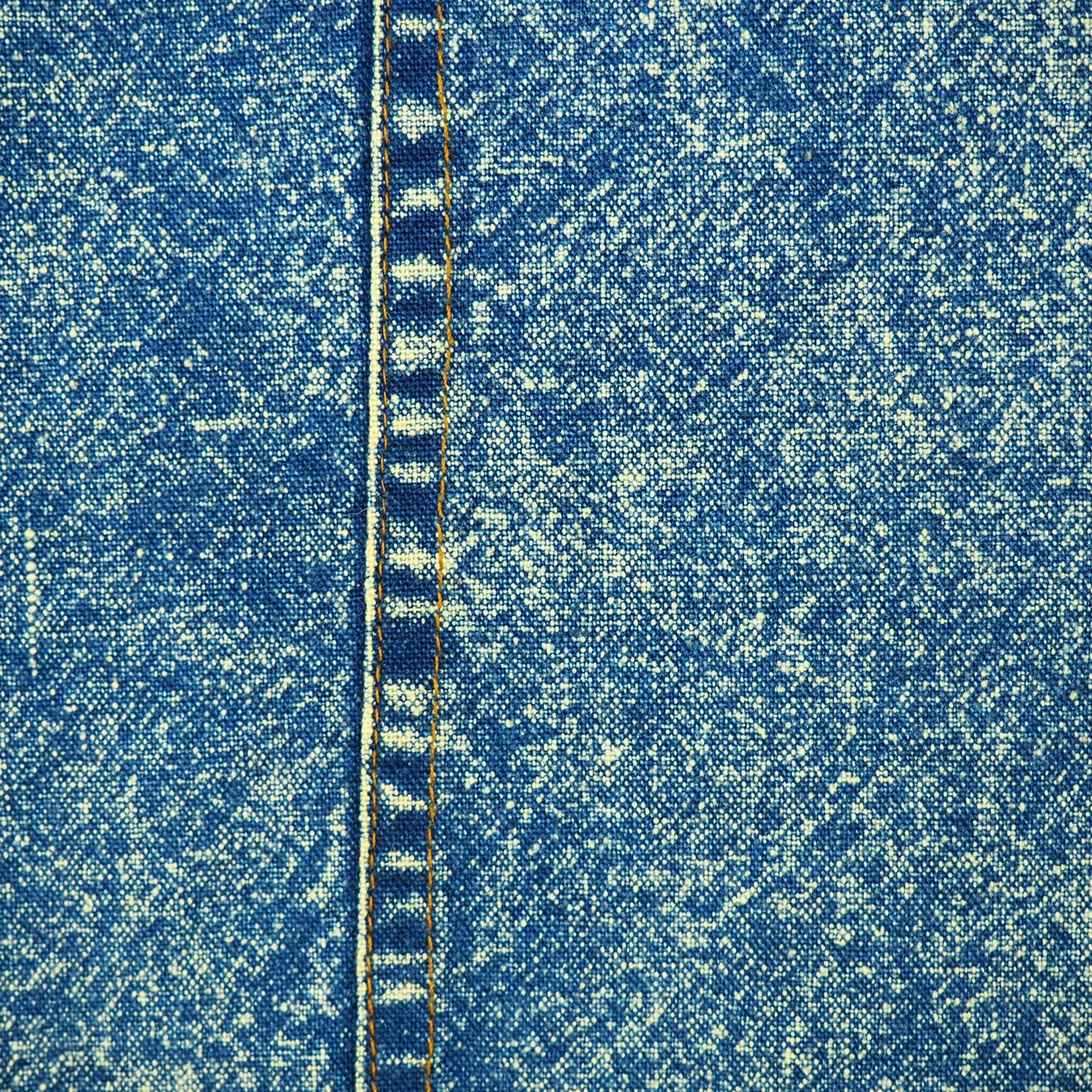 Close-up of blue acid wash denim fabric and seam with orange stitching