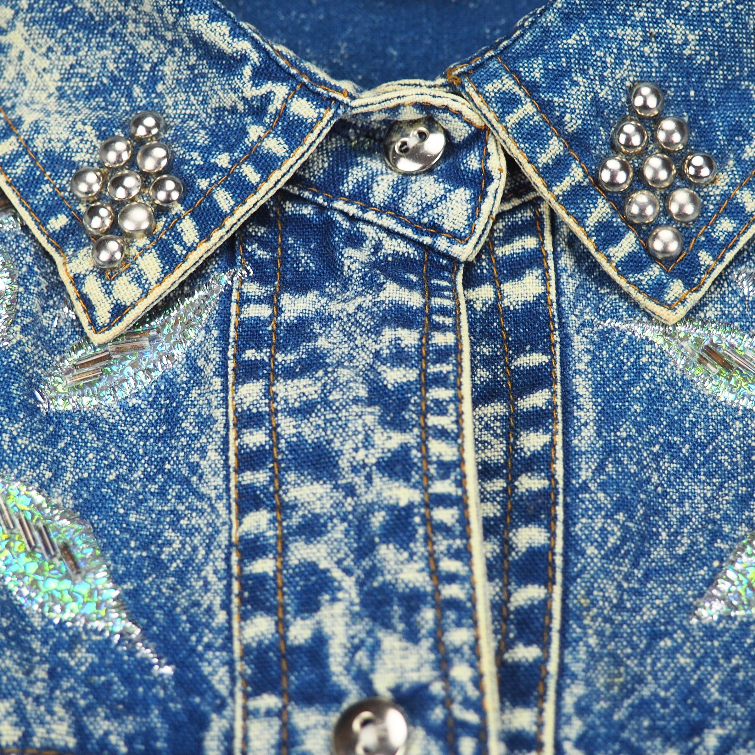 Close-up of a 90s western style acid wash blue denim jshirt collar with decorative buttons, embroidery and stitching.