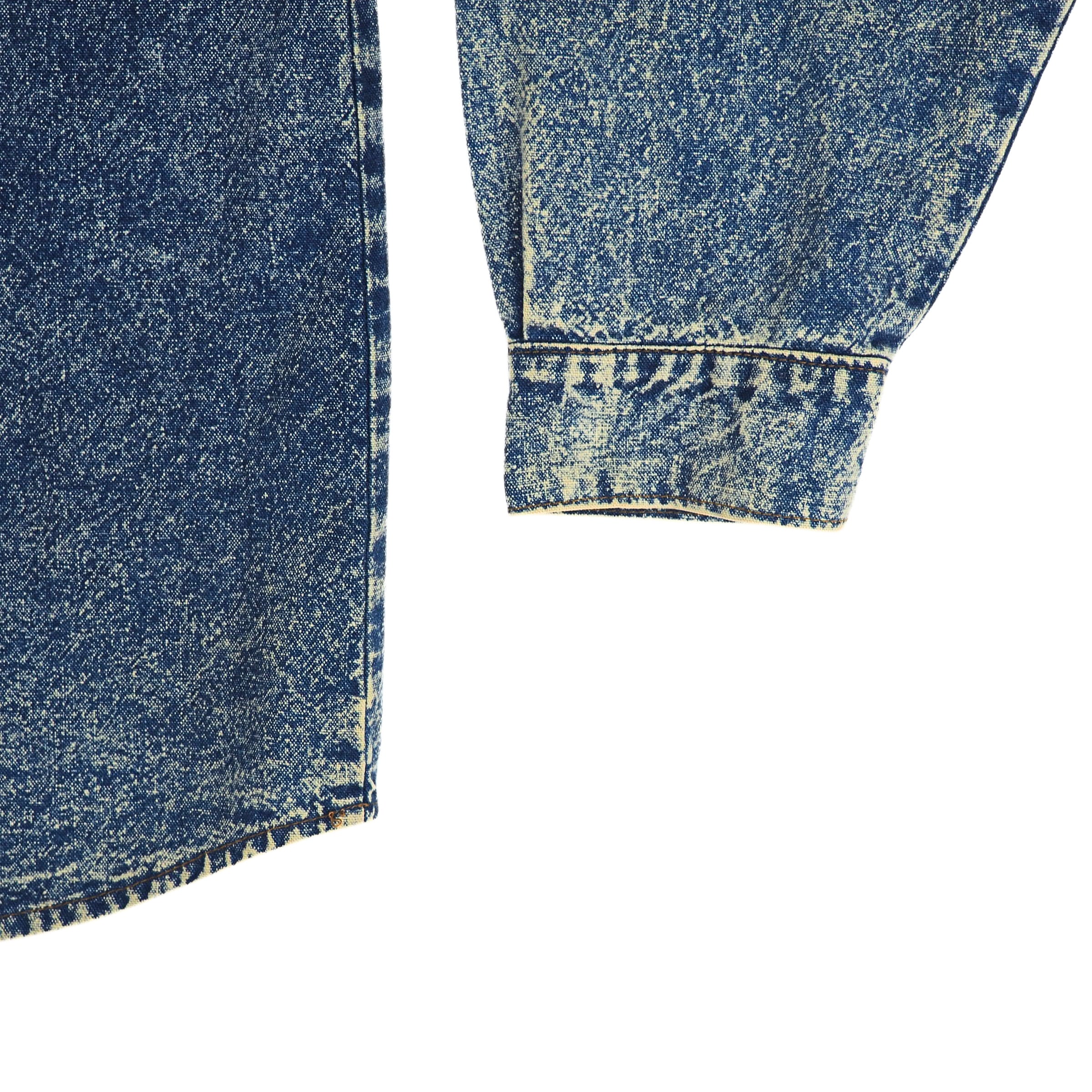 Close-up of blue denim shirt sleeve cuff and tail with a white background